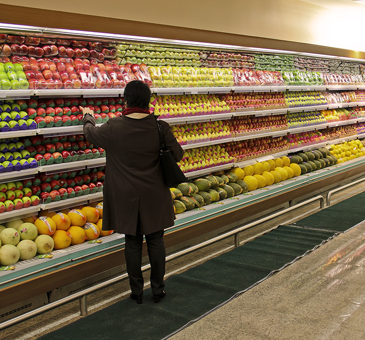 Woman in a grocery store in the produce aisle picking up produce.